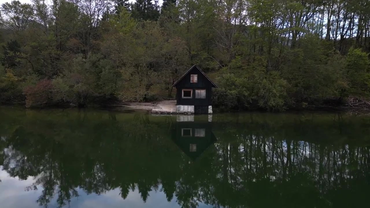Tranquil scene of isolated wooden cabin on still forest lake, with pine trees and peaceful reflections in the water.