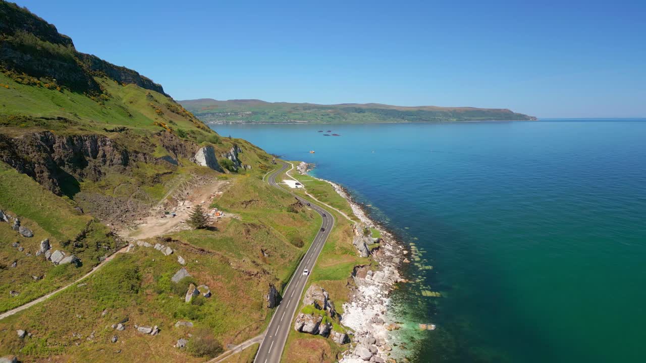 Wide, reversing aerial video of the Causeway Coastal Route at Glenarm in County Antrim, Northern Ireland, UK on a bright and sunny day. Filmed in 4K, 60FPS and with Rec709 color.