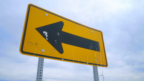 Wind-turbine-generator-on-green-farm-field.-Road-sign-pointing-on-wind-turbines