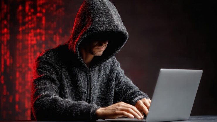 Un misterioso hacker con una felpa scura con cappuccio impegnato in un'operazione digitale su un laptop, circondato da rappresentazioni di codice rosso incandescente e ombre del mondo cibernetico