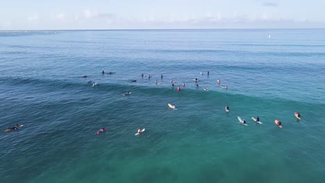 Movimiento-Lento-Sobre-Un-Gran-Grupo-De-Surfistas-En-La-Parte-Superior-Del-Agua-Azul-Cristalina-En-La-Playa-De-Waikiki-En-Honolulu-Hawaii,-Inclinación-Aérea-Del-Carro