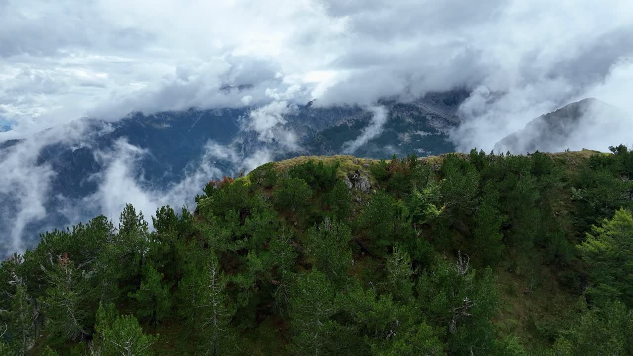 Aerial of Theth Albania rolling hills and dense forests on ridge, mist and cloud breathing drifting over the landscape