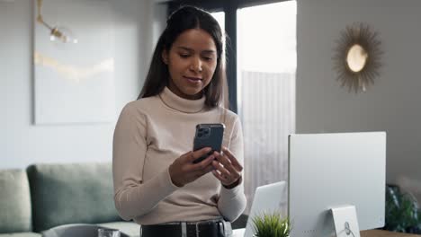 Mujer-De-Raza-Mixta-Sentada-En-El-Escritorio-Y-Navegando-Por-Teléfono