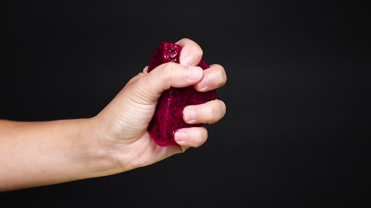 la mano exprimiendo la fruta del dragón, el jugo goteando