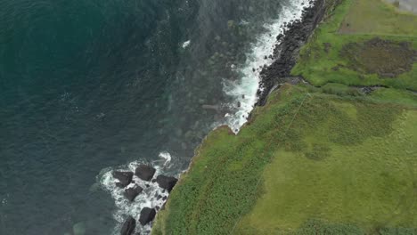 drone shot of waterfall ending in a sea cliff in isle of skye scotland, green grass and clear blue ocean water