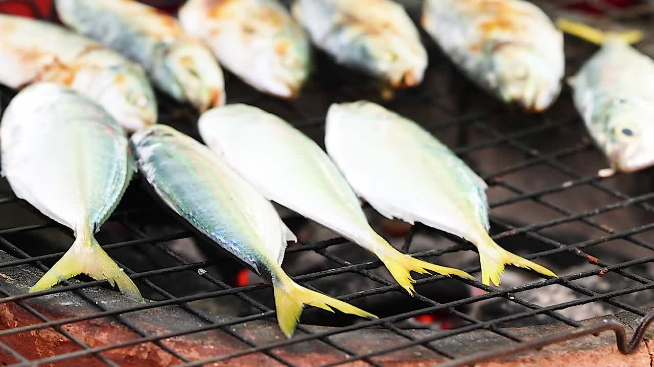 Close-up of fresh fish being grilled on a charcoal barbecue, showcasing their golden-brown texture.