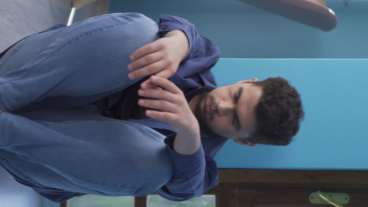 vídeo vertical de un hombre deprimido. se sienta junto a la pared.