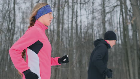 un hombre y una mujer jóvenes corren por la mañana en el bosque de invierno. una mujer con una chaqueta holgada y un hombre con una chaqueta negra corre por un parque de invierno. estilo de vida saludable familia feliz.