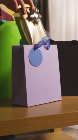 video vertical de una persona tomando regalos de bolsas de regalos en la mesa en la sala de estar