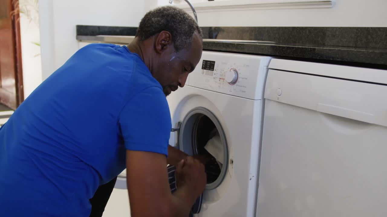African american senior man putting dirty laundry into washing machine at home
