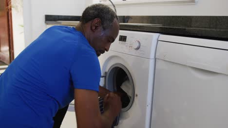 African-american-senior-man-putting-dirty-laundry-into-washing-machine-at-home