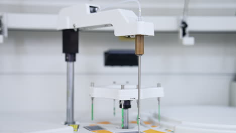 machine detail is moving lowering and going up. advanced equipment performing science medical analysis and testing. close up. blurred backdrop.