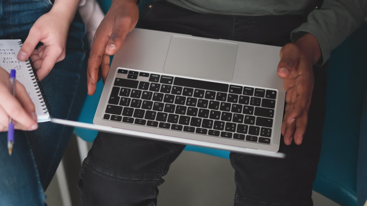hombre negro con computadora portátil en el regazo en el interior de primer plano. empleado afroamericano utiliza computadora moderna sentado con un colega en la oficina. tipo trabaja en línea a través de un dispositivo