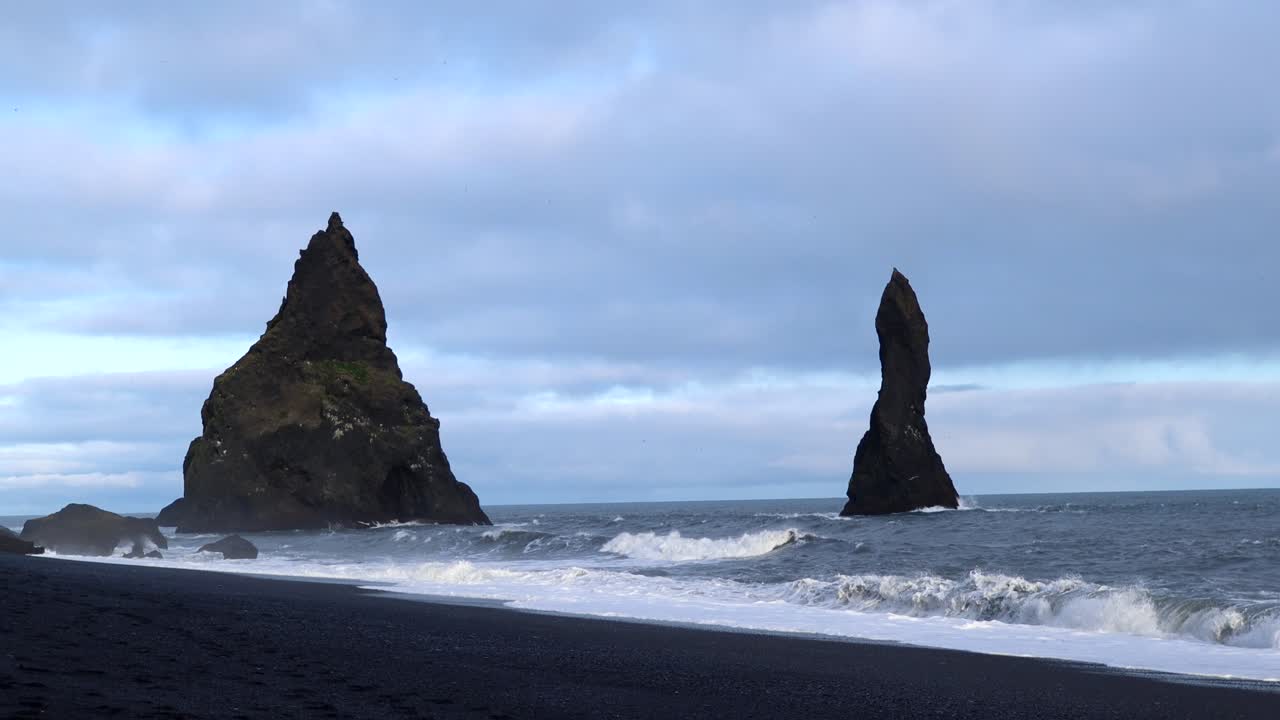 hermosas rocas en el agua en la playa de arena negra reynisfjara en islandia, 4k