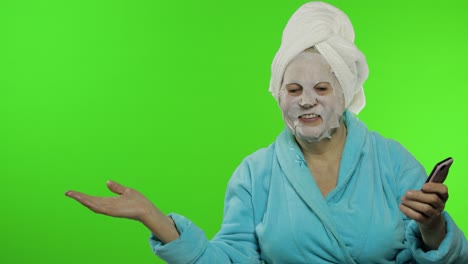 Abuela-En-Bata-De-Baño,-Mascarilla.-Mujer-Con-Teléfono-Inteligente-Apuntando-A-Algo