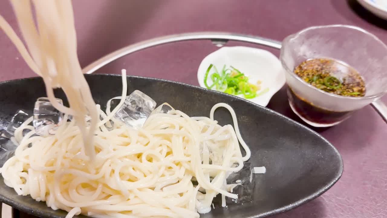 冷たいうどん麺を金属製のトングで美味しいつけ汁に浸す手のクローズアップショット