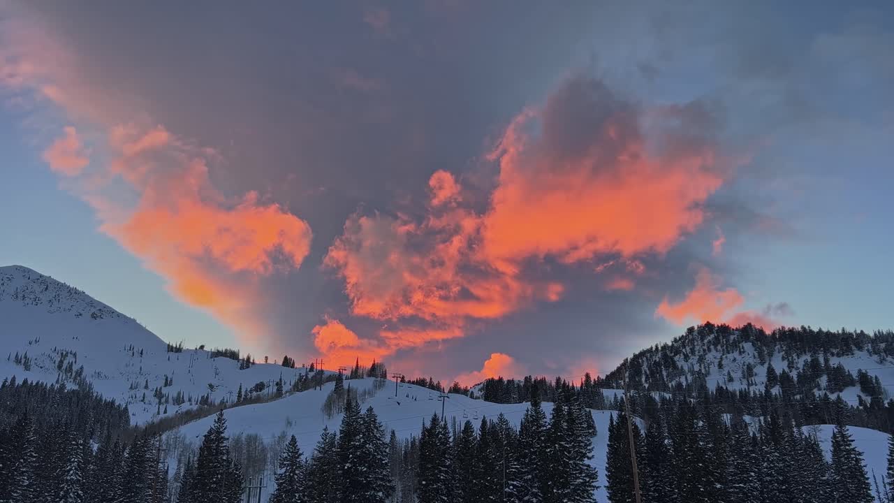 Stunning winter sunset with vivid orange and pink colors above a large ski resort in the Rocky Mountains of Utah on a cold winter evening