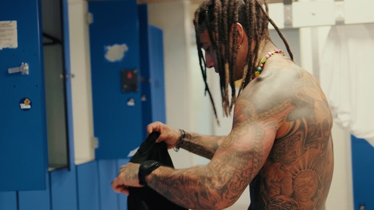 Tattooed Man with Dreadlocks Changing Clothes in a Locker Room