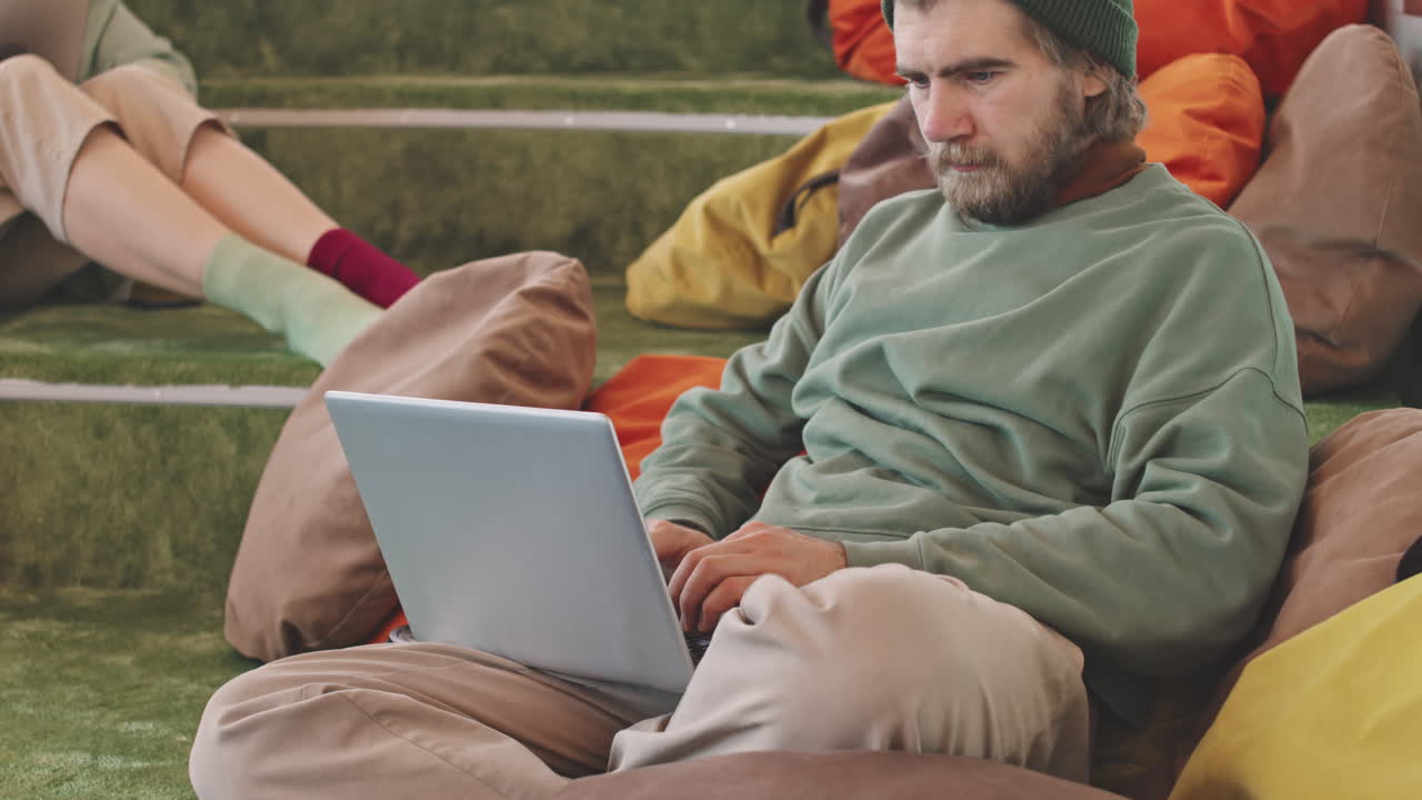 Hipster Working on Laptop in Lounge Area of Coworking Space