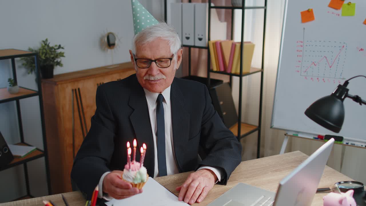 anciano empresario celebrando su cumpleaños en la oficina sosteniendo un pequeño pastel con velas haciendo un deseo