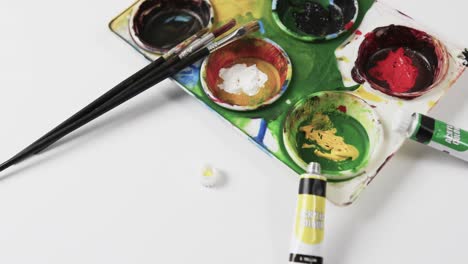 close up of paints and brushes on white background, in slow motion