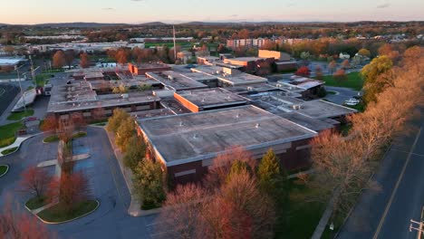 Aerial-approaching-shot-of-american-school-and-colorful-trees-lighting-by-sunset-light