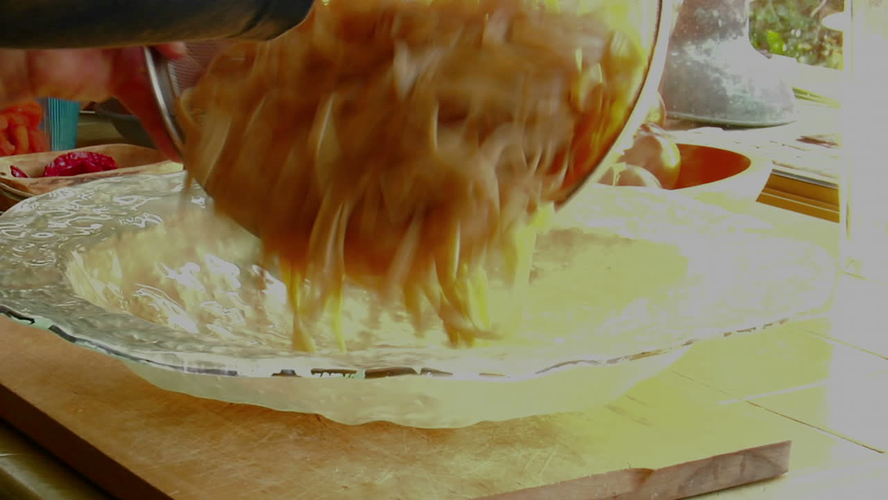 한 여성 요리사가 갓 조리한 파스타를 유리 그릇에 부어 식사를 준비합니다.