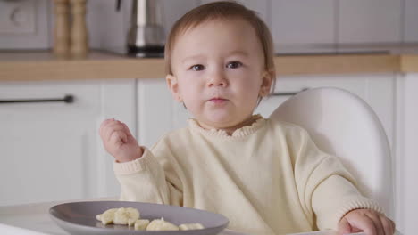 Cute-Baby-Girl-Eating-Banana-Slices-Sitting-In-Her-High-Chair-In-The-Kitchen-6