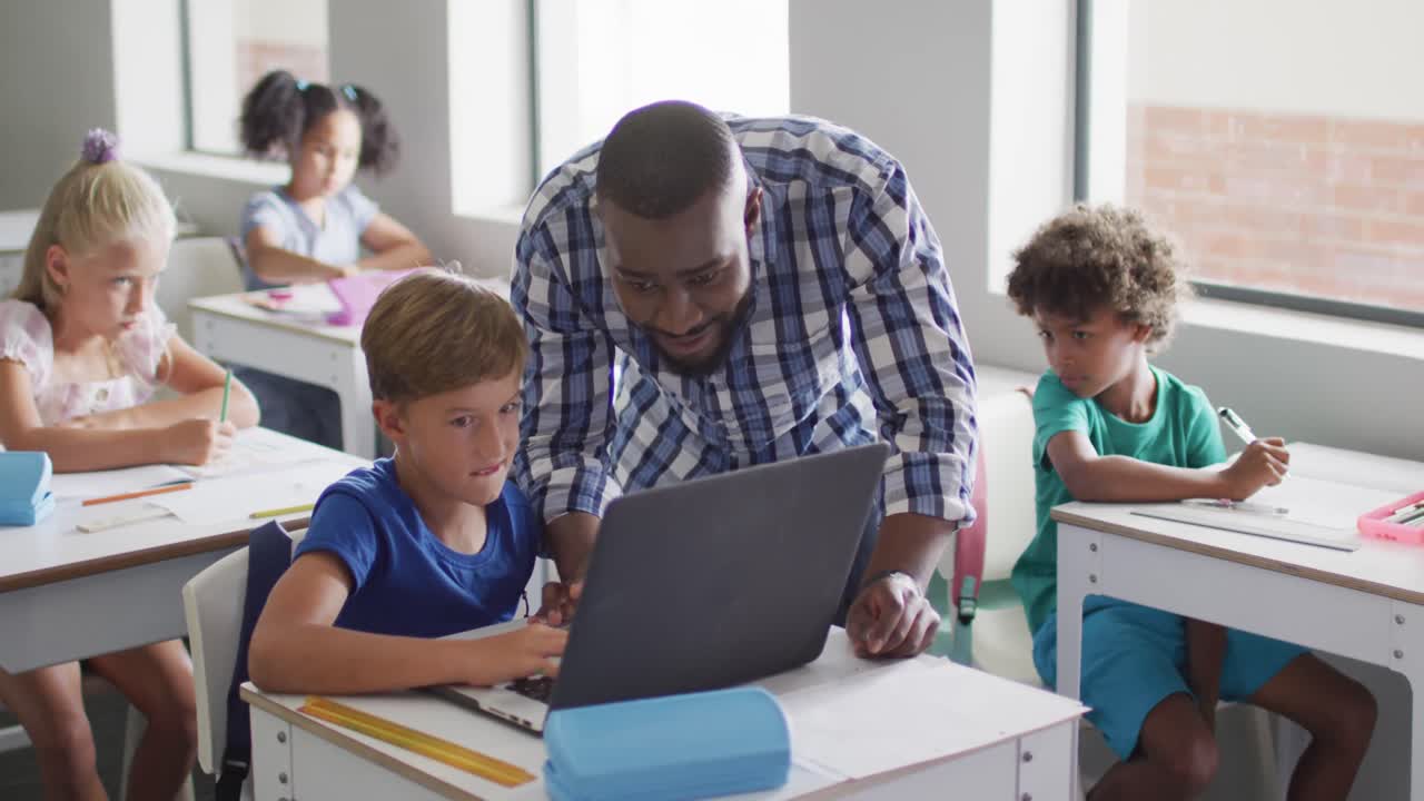 Video of happy african american male teacher helping caucasian boy with laptop