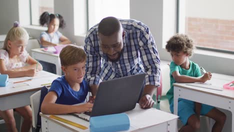 video of happy african american male teacher helping caucasian boy with laptop