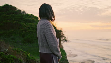 Woman-enjoy-ocean-twilight-walking-on-coast-hill-holding-album.-Gloomy-nature