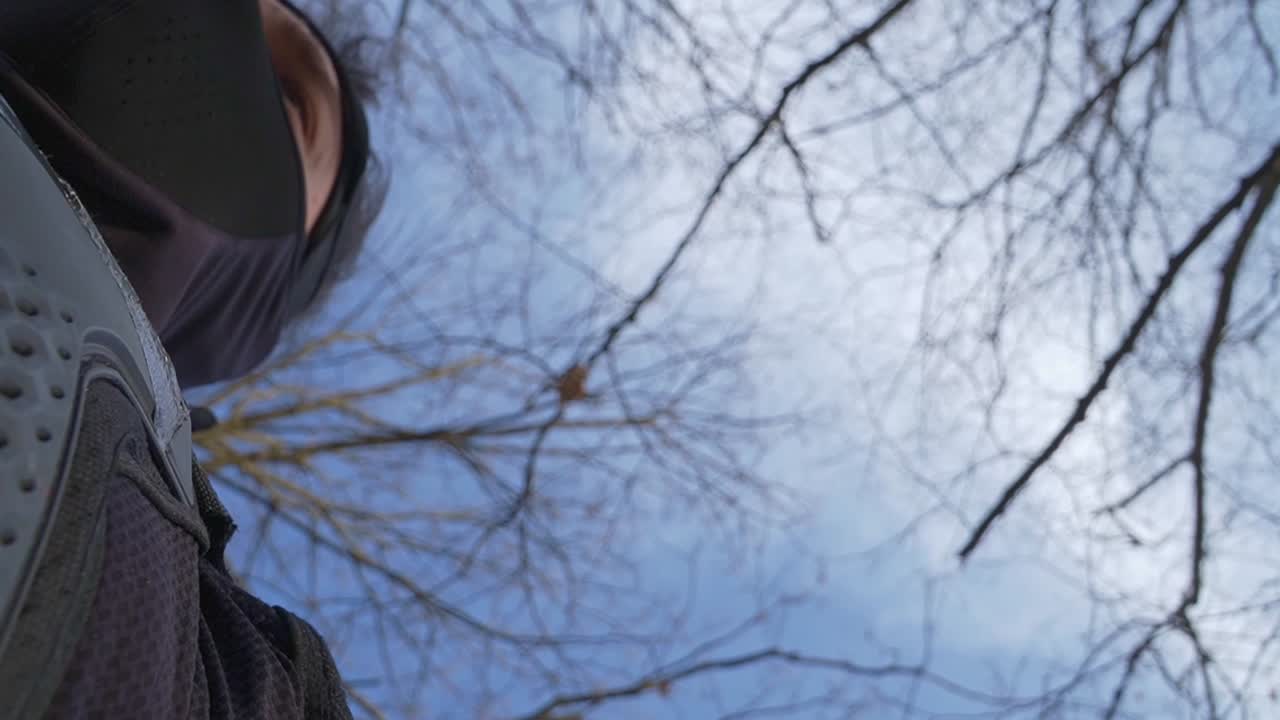 A dramatic low-angle shot of a ninja in black armor gazing at the sky, surrounded by bare tree branches. The cinematic perspective adds mystery and tension, ideal for action and storytelling