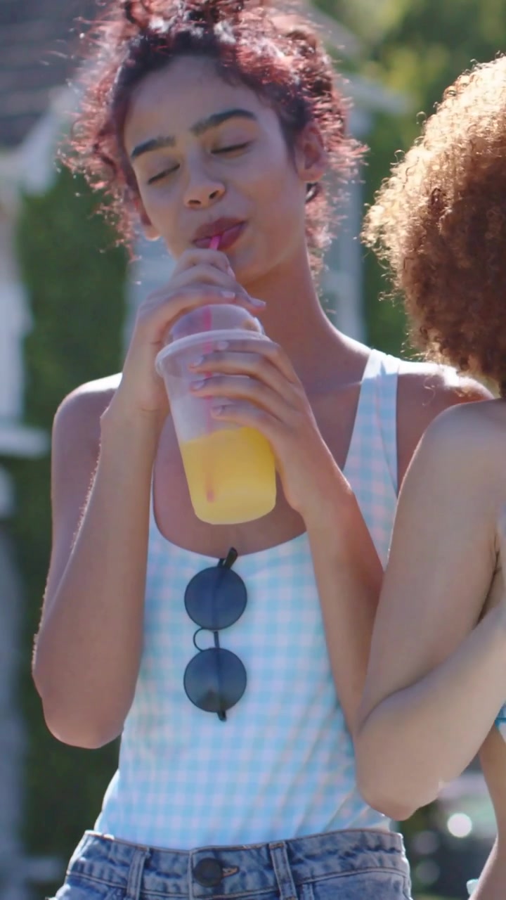 Video vertical: Al ver llegar a una amiga, mujer en traje de baño de cuadros vichy levantando una taza, bebiendo para refrescarse en el patio