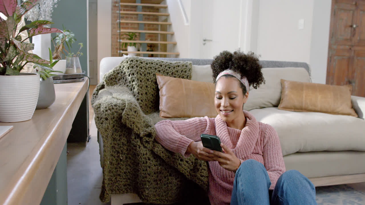 Happy biracial woman using smartphone at home, slow motion