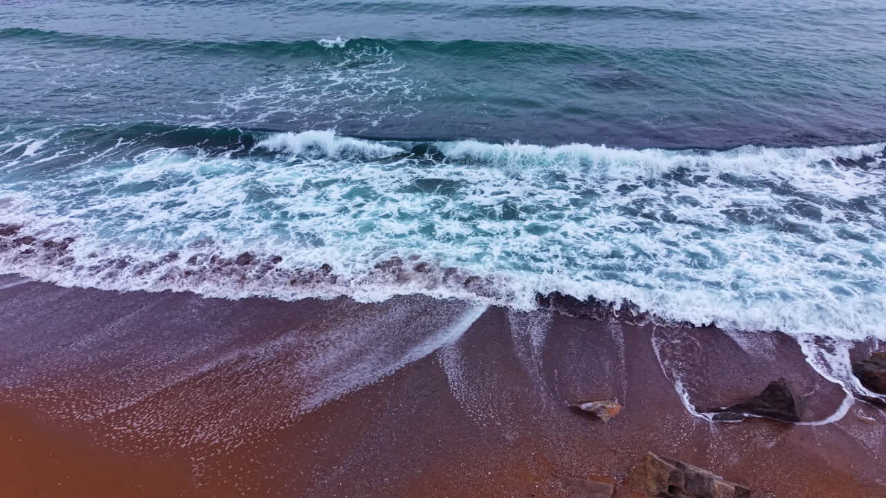 Onde che si infrangono su una spiaggia sabbiosa durante il giorno, vicino all'oceano, sotto un cielo nuvoloso in una località costiera