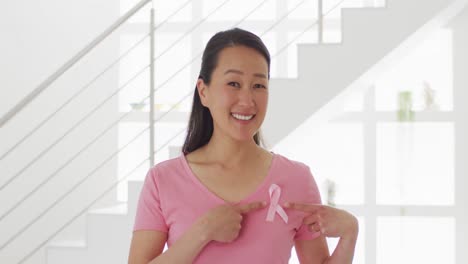 happy asian woman in pink tshirt showing pink ribbon at home