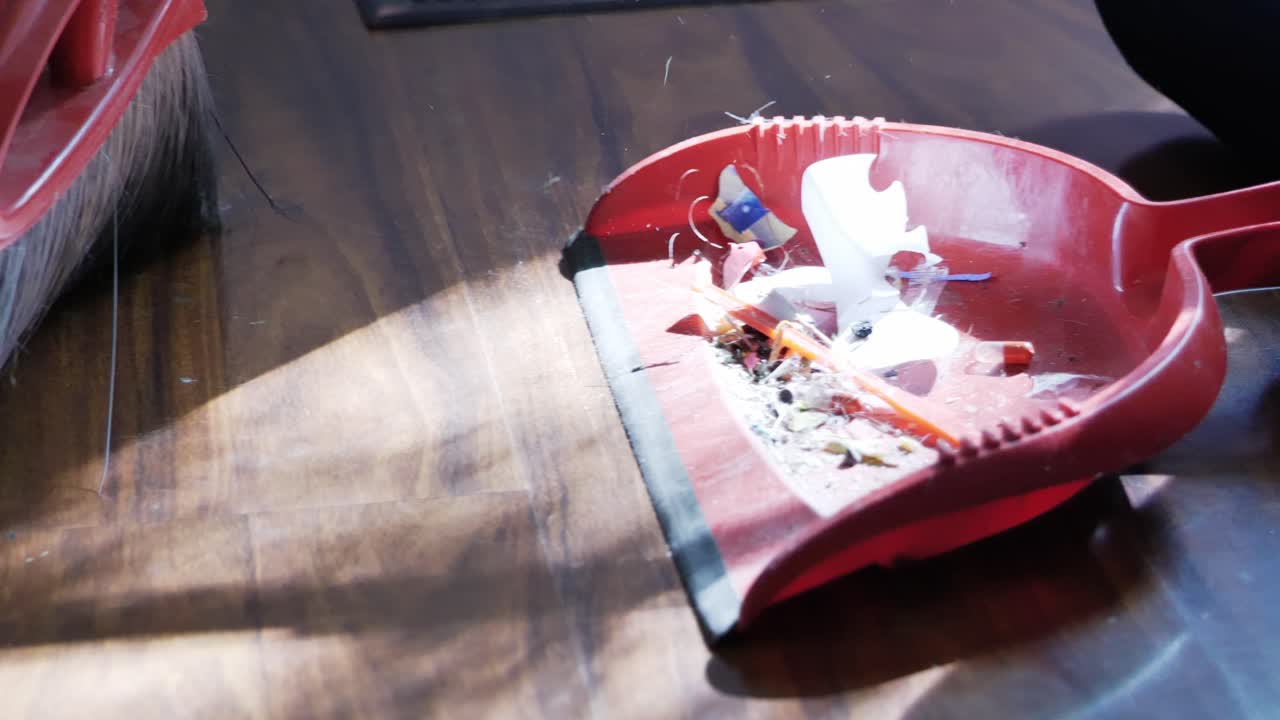 더러운 갈색 나무 바닥을 빨간 빗자루와 함께 먼지 팬으로 쓸고 아이가 코로나19 팬데믹 잠금 측면 각도 클립 동안 그것을 잡는 것을 돕습니다 - in cinema 4k