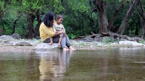 isolated woman spending quality time with son on stone at calm lake shore in the morning