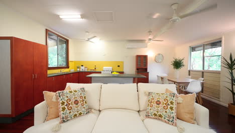 Pullback from Beige Couch on Braided Rug in Colourful House With Wooden Floorboards And Cabinets, Open Plan Kitchen and Loungeroom. Interior of home for real estate property.