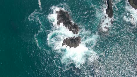 Aerial-top-down-over-sea-waves-crashing-on-rocky-coast-near-Menganti-beach,-Kebumen-in-Indonesia