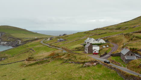 Car-passing-around-houses-in-countryside.-Narrow-coastal-road-between-green-pastures-above-sea.-Ireland