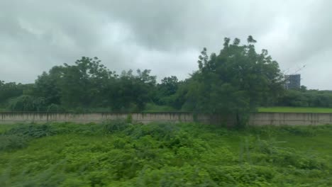 breathtaking view of lush greenery enveloped in raindrops, as seen from moving train, with dark, cloudy skies enhancing serene and refreshing atmosphere.