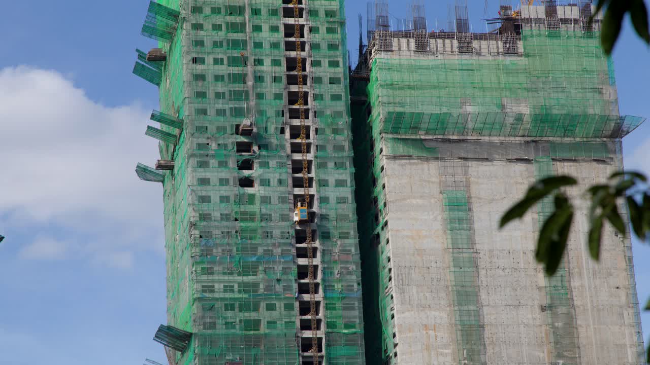 Um arranha-céu de concreto em construção em Manila com rede de segurança verde e um elevador em movimento.