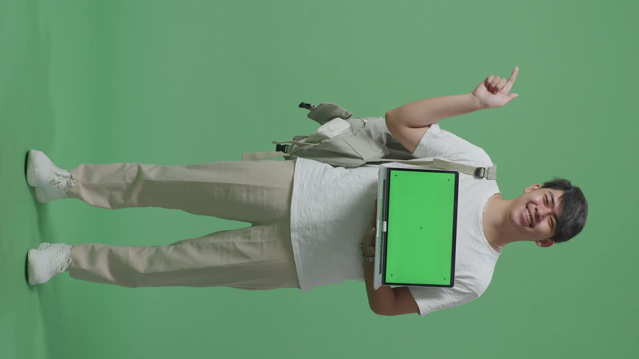 cuerpo lleno de estudiante hombre asiático mostrando simulacro de portátil pantalla verde y dedos directos lado en pantalla verde estudio