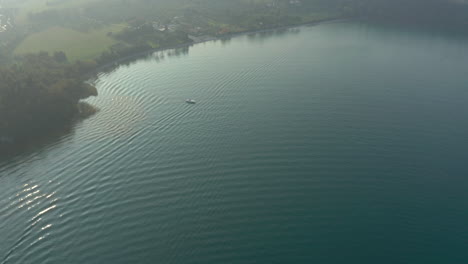 Aerial-shot-following-a-small-boat-that-leaves-a-scenic-harbor-at-Lake-Garda,-Italy