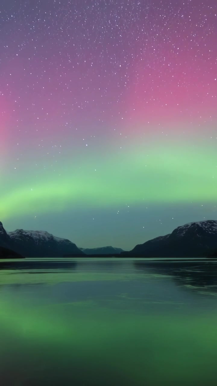 Video verticale: Aurora boreale che si intensifica e si sposta con l'arrivo del vento solare, riflettendosi su un lago di montagna.