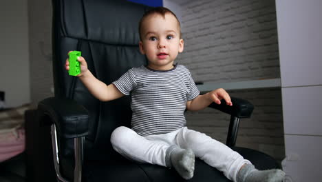 adorable toddler boy sitting in the black leather chair. cute child playing with a brick.