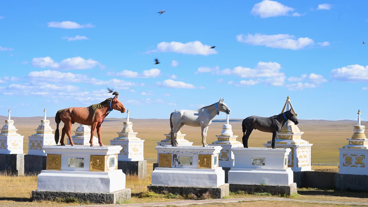 Horse statues atop ornate monuments stand proudly under a clear blue sky in Mongolia. This sacred site honors champion horses, reflecting the deep equestrian culture of the Mongolian steppe