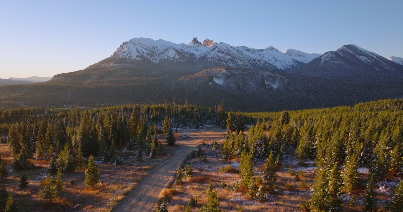 Sunlit mountain peaks above pine forest and valley near Cooke City Montana, alpenglow spreads golden hour light at sunset