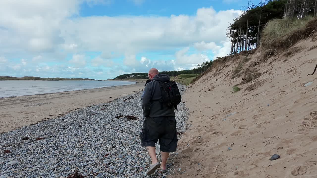 siguiendo a un hombre caminando con su perro mascota en una hermosa playa de arena galesa para hacer ejercicio por la mañana temprano